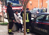 La proprietaria dell'auto seduta su una fioriera ancora spaventata mentre viene consolata dai vigili del fuoco e dai carabinieri.